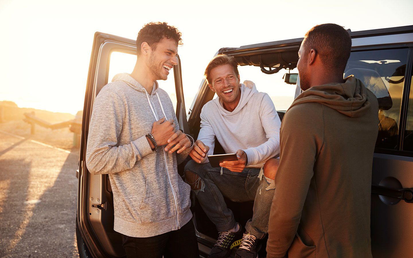 Three men are laughing while standing in the back of a car.